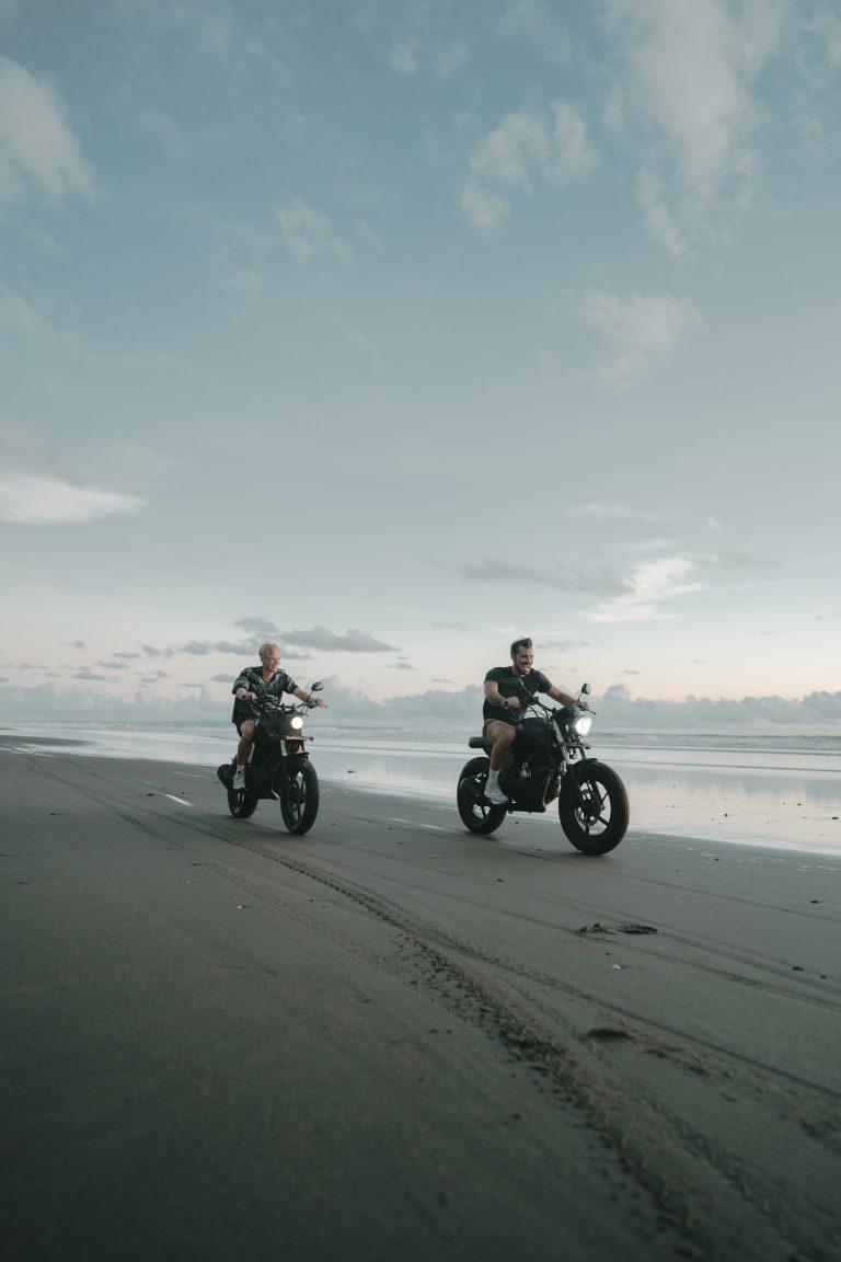 Zwei Jungs die mit dem Motorrad am Strand von Bali fahren beim Sonnenuntergang